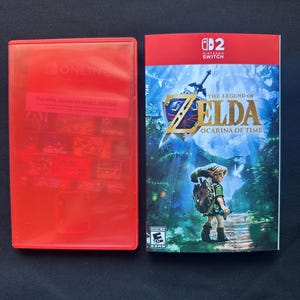 May include: A red plastic Nintendo Switch game case and a game cover insert for The Legend of Zelda: Ocarina of Time. The cover features a character in a forest, the game title in gold text, the Nintendo Switch logo, and an ESRB rating of Everyone 10+.