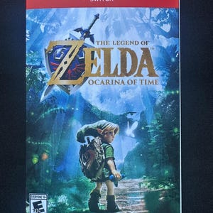 May include: A Nintendo Switch game case cover for The Legend of Zelda: Ocarina of Time. The artwork features a character in green clothing standing on a path, a sword and shield emblem, and the ESRB Everyone 10+ rating logo in the corner.
