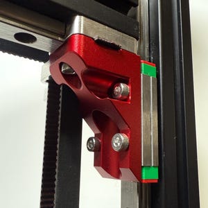 Peut inclure: Gros plan sur un composant métallique rouge avec des boulons argentés, faisant partie d'une machine. Le composant a une finition texturée et est fixé à une courroie noire et à un rail argenté. Des accents verts et rouges sont visibles.