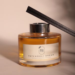May include: A glass air freshener bottle with a silver cap, filled with a golden liquid. The label reads "Patchouli Dream" and "Bamboo Stick Air Freshener." Black diffuser sticks are inserted into the bottle.