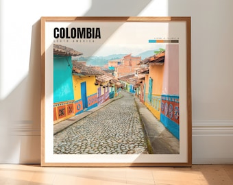May include: A framed print depicting a colourful street scene in Colombia, South America. The street is lined with brightly coloured buildings, and the cobblestone road leads up a hill.