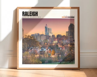Può includere: Una stampa incorniciata dello skyline di Raleigh, Carolina del Nord, al tramonto. Lo skyline della città è visibile in lontananza, con alberi e case in primo piano. La stampa ha una tavolozza di colori rosa, arancio e blu.