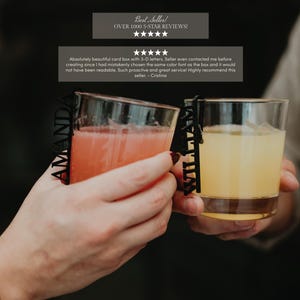 May include: Two clear glass tumblers filled with colored beverages, each featuring a black vertical name tag attached to the rim. One tag displays the name AMANDA in capital letters, while the other tag displays the name WILLIAM in capital letters.