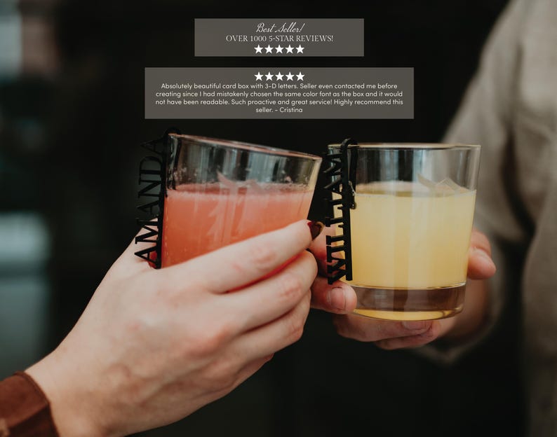 May include: Two clear glass tumblers filled with colored beverages, each featuring a black vertical name tag attached to the rim. One tag displays the name AMANDA in capital letters, while the other tag displays the name WILLIAM in capital letters.