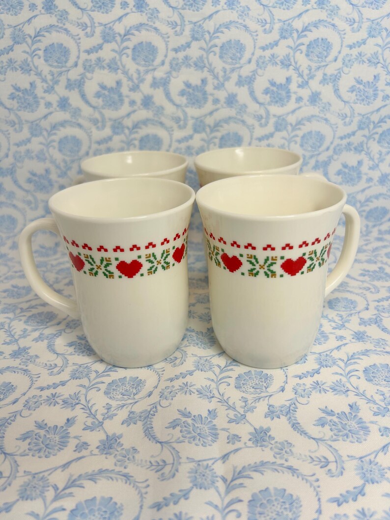 May include: Set of four white ceramic mugs with a red and green heart pattern. The mugs have a simple design and are perfect for everyday use.