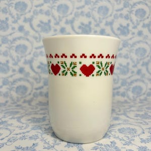 May include: White ceramic mug with a red, green, and yellow geometric pattern featuring hearts.