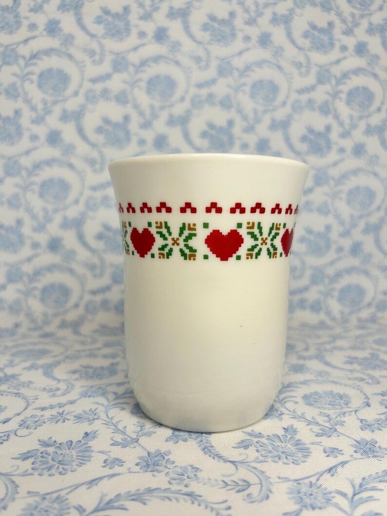 May include: White ceramic mug with a red, green, and yellow geometric pattern featuring hearts.