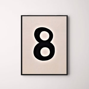 May include: A framed art print featuring a large, black number eight against a light beige background. The number is bold and rounded, with a minimalist design. The frame is black, creating a striking contrast.