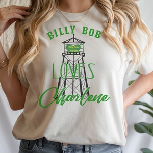 May include: White t-shirt with green text that reads "Billy Bob Loves Charlene" and a black and white illustration of a water tower with the text "Billy Bob Charlene" on it.