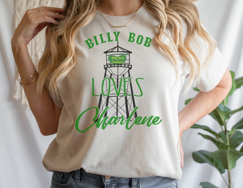 May include: White t-shirt with green text that reads "Billy Bob Loves Charlene" and a black and white illustration of a water tower with the text "Billy Bob Charlene" on it.