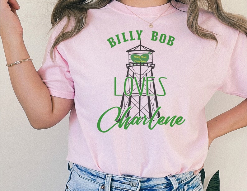 May include: Pink t-shirt with a graphic of a water tower that says "Billy Bob Loves Charlene" in green text.