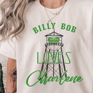 May include: White t-shirt with a green and black graphic of a water tower with the text "Billy Bob Loves Charlene" and a heart that says "Billy Bob Charlene".