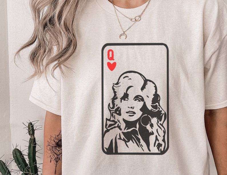 Peut inclure: T-shirt cr&egrave;me avec un motif de carte &agrave; jouer repr&eacute;sentant le portrait d'une femme et le symbole de c&oelig;ur rouge et la lettre "Q". Le graphisme est en noir et blanc.