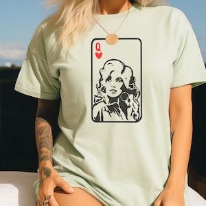 Peut inclure: T-shirt vert clair avec un motif de carte &agrave; jouer en noir et blanc. La carte repr&eacute;sente un portrait de femme, le symbole de c&oelig;ur rouge et la lettre "Q" pour Reine.