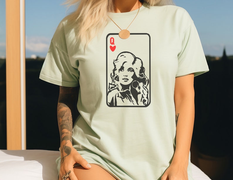 Peut inclure: T-shirt vert clair avec un motif de carte &agrave; jouer en noir et blanc. La carte repr&eacute;sente un portrait de femme, le symbole de c&oelig;ur rouge et la lettre "Q" pour Reine.