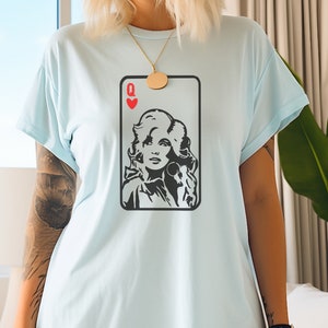 Peut inclure: T-shirt bleu clair avec un motif de carte &agrave; jouer. La carte est une Reine de C&oelig;ur, avec un portrait noir et blanc d'une femme. Le t-shirt a des manches courtes et une coupe ample.