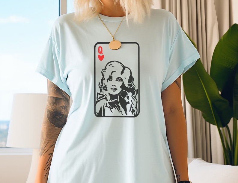 Peut inclure: T-shirt bleu clair avec un motif de carte &agrave; jouer. La carte est une Reine de C&oelig;ur, avec un portrait noir et blanc d'une femme. Le t-shirt a des manches courtes et une coupe ample.