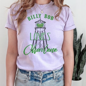 May include: A lavender t-shirt with a graphic of a water tower that says "Billy Bob Loves Charlene" in green text.