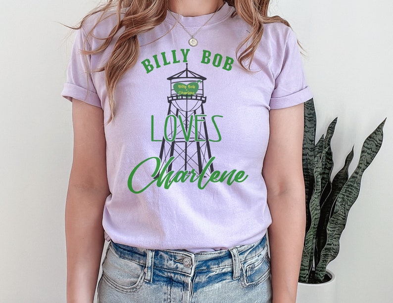 May include: A lavender t-shirt with a graphic of a water tower that says "Billy Bob Loves Charlene" in green text.