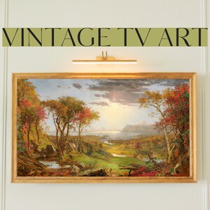 May include: A vintage TV screen displaying a painting of a landscape with trees, a river, and mountains in the distance. The painting is set in a golden frame.
