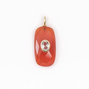 May include: A faceted, orange-red gemstone pendant with a gold bail. The pendant has an oval, clear gemstone set in a gold bezel. The pendant is displayed on a white background.