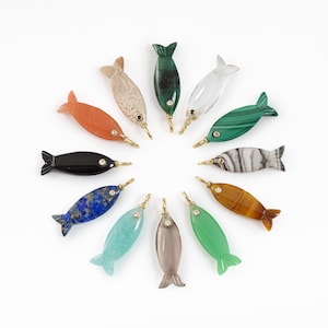 May include: A collection of twelve gemstone fish pendants in various colors, including orange, green, blue, and black, arranged in a circle on a white background. Each fish has a gold-colored bail and a small gem accent.