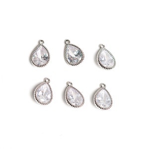 May include: Six silver teardrop-shaped charms with clear crystal accents. The charms have a beaded edge and are perfect for jewelry making.
