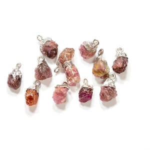 May include: A collection of pink and red gemstone pendants with silver accents. The gemstones are rough and natural, with a variety of shapes and sizes.