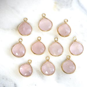 May include: Ten pink rose quartz gemstone pendants with gold-toned metal settings. The pendants are shaped like teardrops and have a faceted finish.