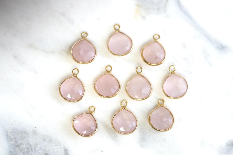 May include: Ten pink rose quartz gemstone pendants with gold-toned metal settings. The pendants are shaped like teardrops and have a faceted finish.