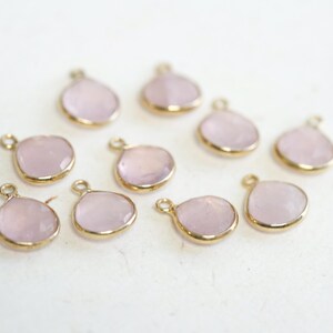 May include: Ten pink gemstone charms with gold-toned metal settings. The charms are shaped like teardrops and have a smooth, polished finish.