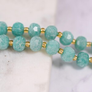 May include: Close-up of two strands of turquoise gemstone beads with gold-colored spacers. The beads have a faceted, irregular shape, and the gold spacers add a touch of elegance. The background is a soft, blurred white and gray.