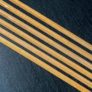 May include: Four gold-colored, herringbone chain necklaces on a black background.