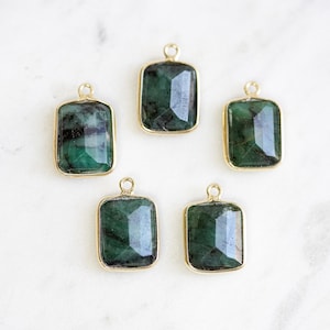 May include: Five emerald green gemstone pendants with gold settings. The pendants are rectangular in shape and have a faceted finish.