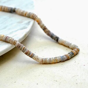 Pu&ograve; includere: Una collana fatta di piccole perline rotonde di colore marrone chiaro, grigio e bianco. Le perline sono infilate su un filo sottile.