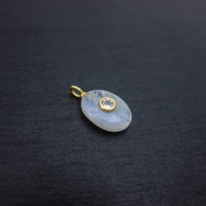 Pu&ograve; includere: Un ciondolo di forma ovale con una pietra bianca lattiginosa e traslucida con sottili sfumature blu. Una piccola gemma rotonda e trasparente &egrave; incastonata in oro nella parte superiore centrale. Un anellino d'oro &egrave; fissato alla sommit&agrave;.