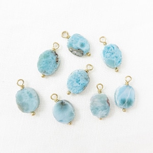 May include: Eight oval-shaped, light blue larimar gemstone pendants with gold-colored wire loops and small gold beads. The pendants are arranged on a white surface.