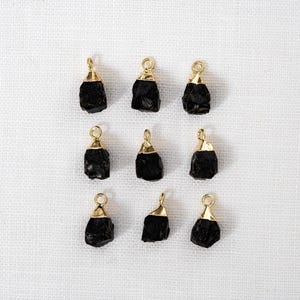 May include: Ten black gemstone pendants with gold-toned jump rings. The gemstones are irregularly shaped and have a rough, natural texture.