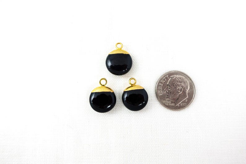 May include: Three black and gold round charms with a small loop at the top for stringing. A coin is next to the charms for size comparison. The charms have a glossy black finish with a gold-coloured cap.