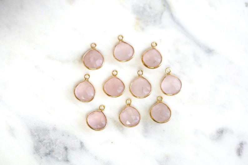 May include: Twelve gold-tone pendants with rose quartz stones. Each pendant is shaped like a teardrop.
