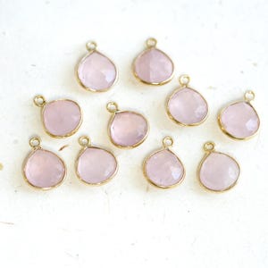 May include: Ten gold-toned pendants with pink gemstone drops. Each pendant has a loop for attaching to a chain or cord.