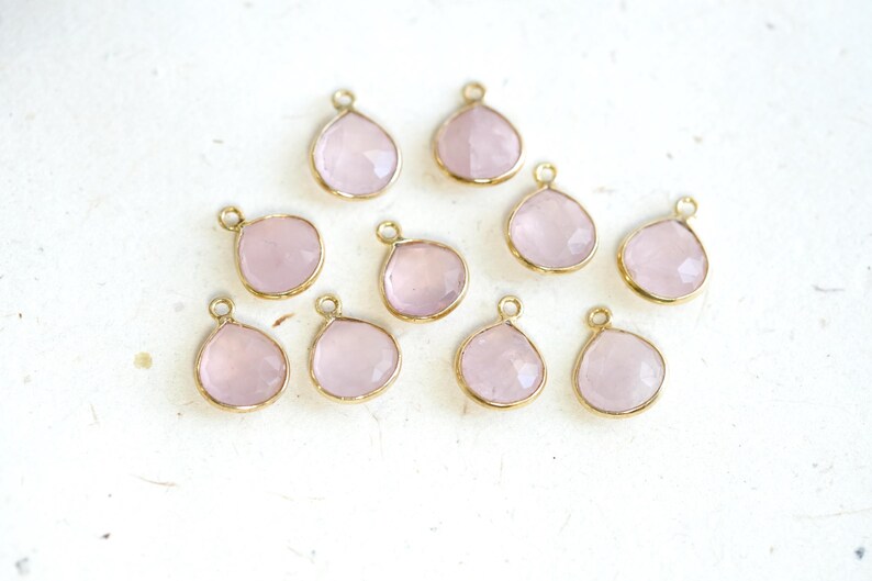 May include: Ten gold-toned pendants with pink gemstone drops. Each pendant has a loop for attaching to a chain or cord.