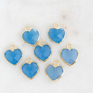 May include: Seven blue heart-shaped charms with gold-toned metal settings. The charms are faceted and have a light blue color.