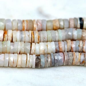 May include: A strand of white, gray, and brown gemstone beads. The beads are faceted and have a slightly irregular shape. They are strung on a clear thread.