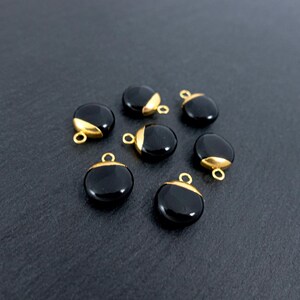 May include: Seven black, round gemstone pendants with gold-coloured caps and small loops. The pendants are arranged on a dark grey surface. The gold caps cover a portion of the top of each pendant.