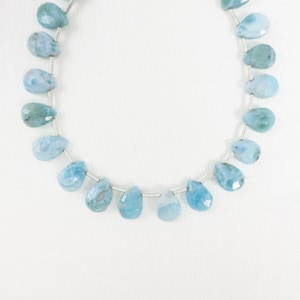May include: Strand of light blue, teardrop-shaped gemstone beads. The beads are strung on a thin, silver-colored wire. The gemstones have a translucent quality and vary in shades of blue and green.
