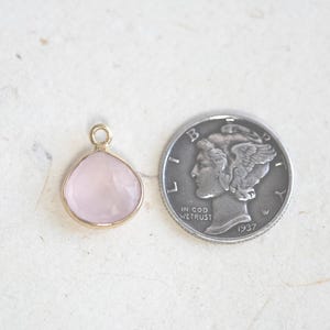 May include: A small, pale pink gemstone pendant with a gold setting. The pendant is about the size of a dime.