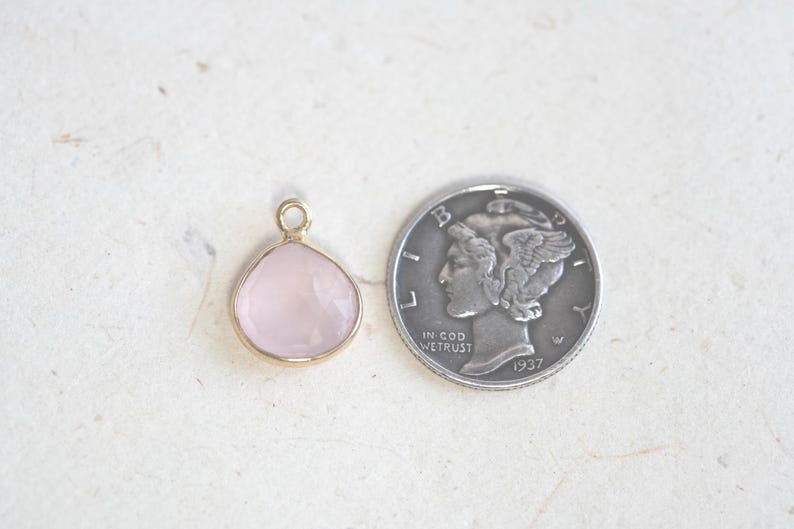 May include: A small, pale pink gemstone pendant with a gold setting. The pendant is about the size of a dime.