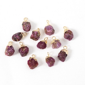 May include: Twelve raw ruby gemstone pendants with gold-plated jump rings. The ruby gemstones are a deep red color and have a rough, natural texture.