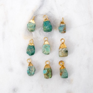 May include: Ten turquoise gemstone pendants with gold accents. The gemstones are irregular in shape and have a rough, natural texture. The pendants are perfect for jewelry making.